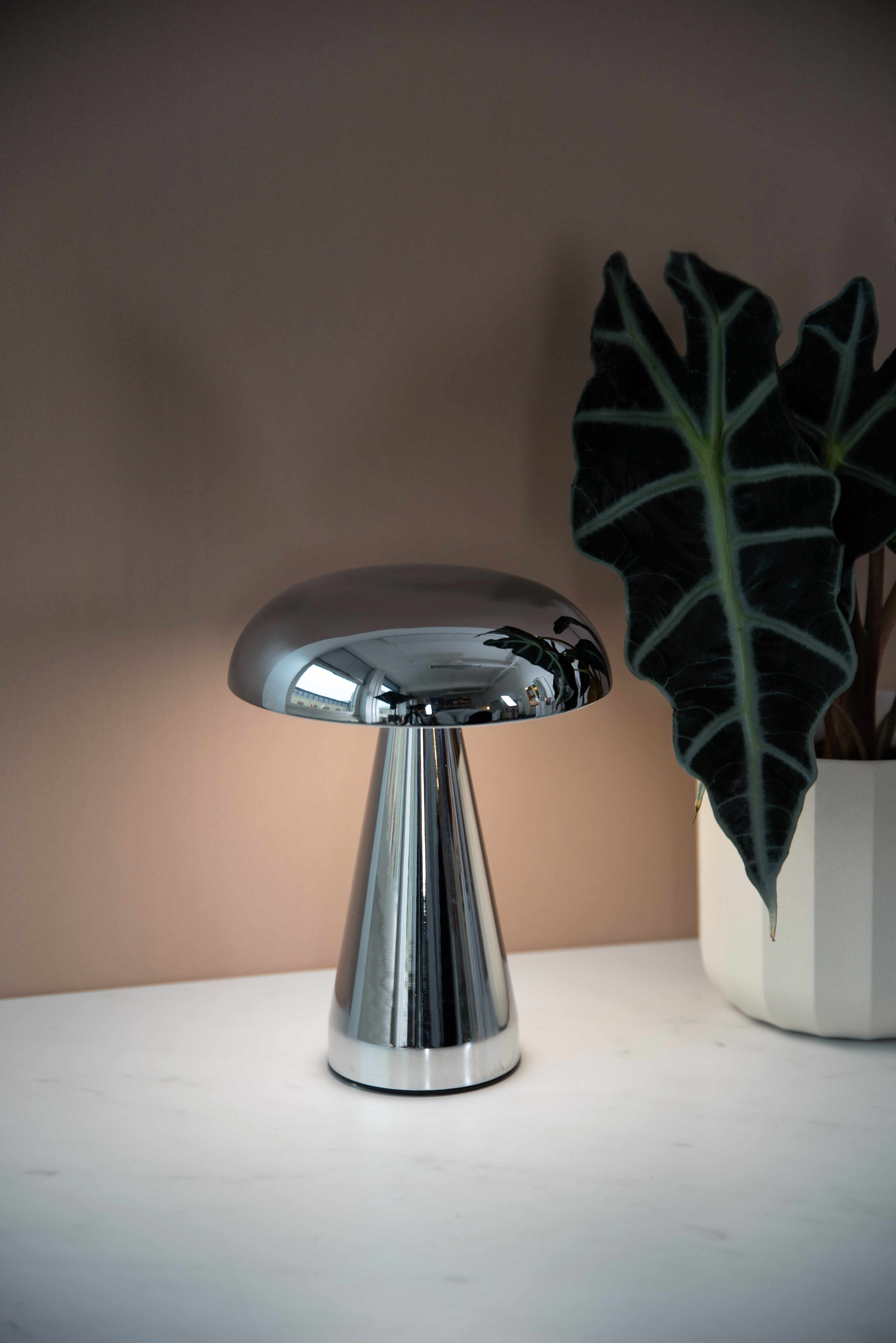 En liten, kromfärgad bordslampa står på ett ljusare underlag.