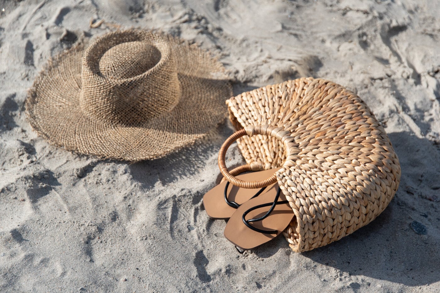 Solhatt, stråveske og sandaler i sanden.