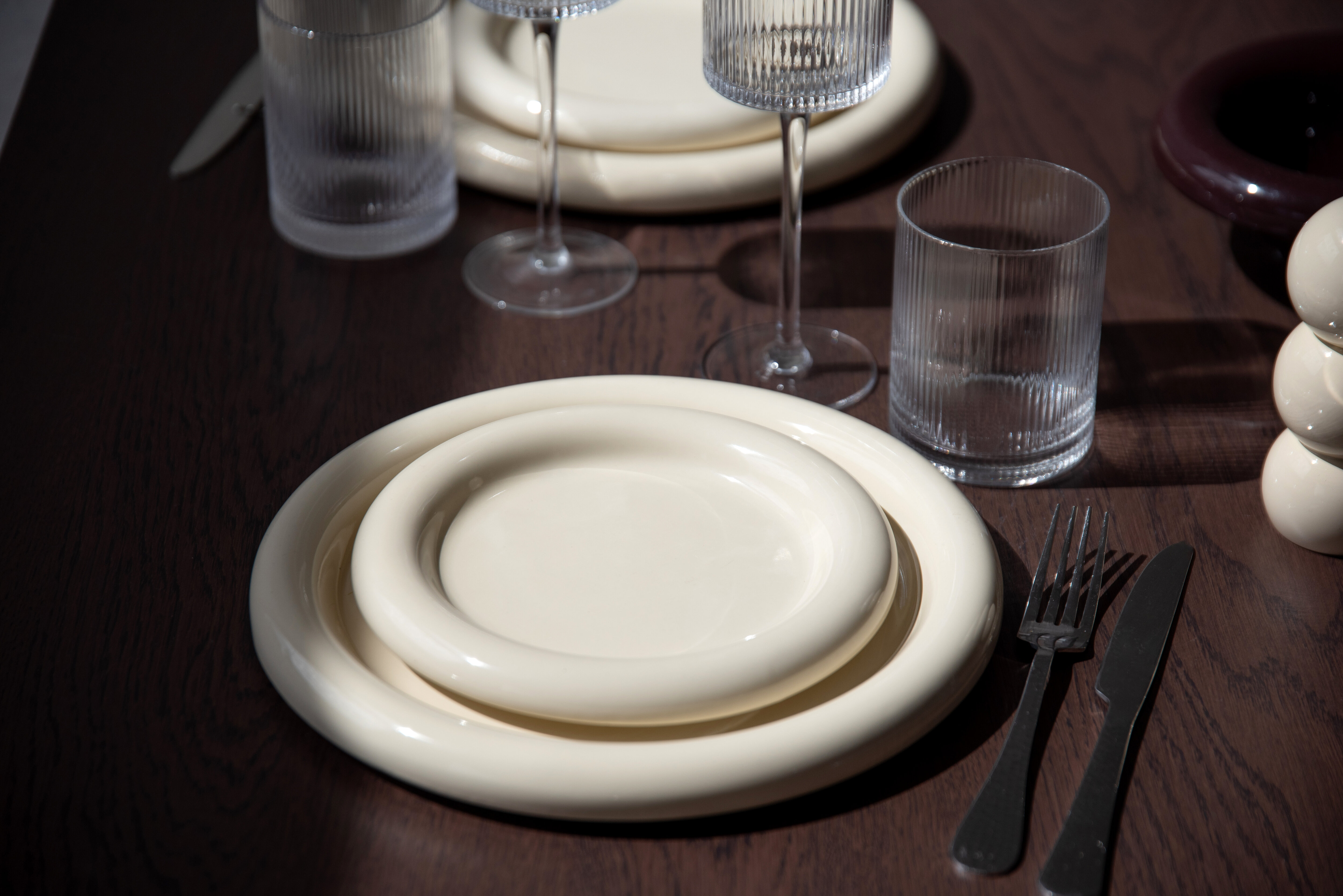 Borddekking med Bullig-tallerkener og glass fra Ribbed-kolleksjonen på et mørkt trebord.