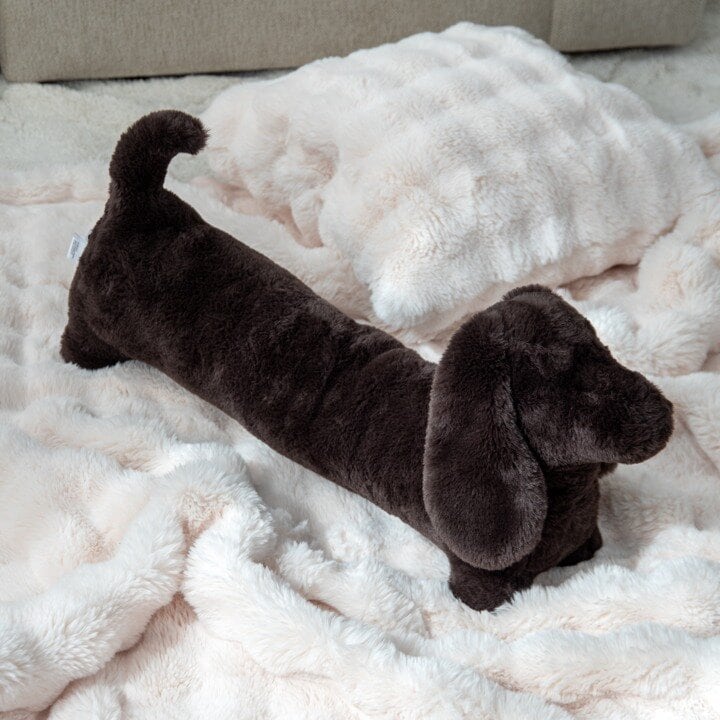 Brun dachshundformet pute på et mykt, lyst pledd.