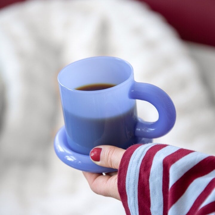 Blå kaffekopp med skål holdes i hånden.