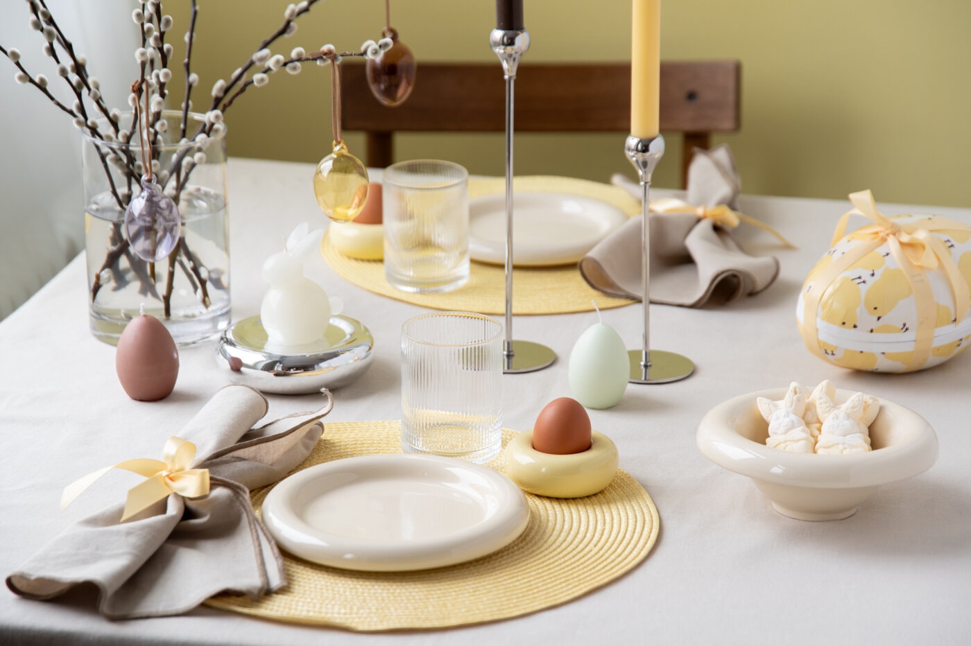 Påskebord dekket i lyse vårfarger med servise, glass og eggedekor