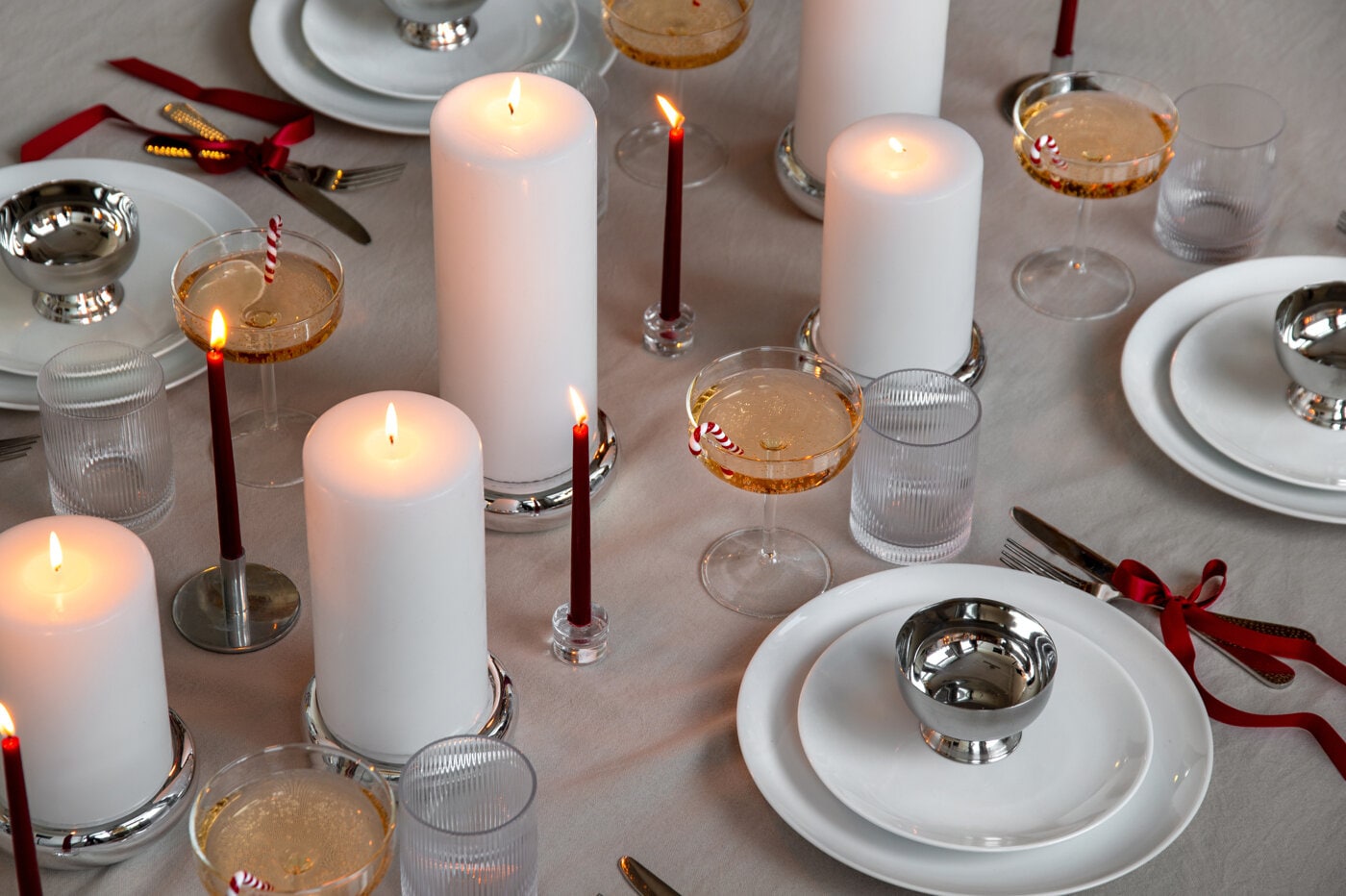 Festlig borddekking med hvite blokklys, smale røde lys og champagneglass dekorert med polkastenger.
