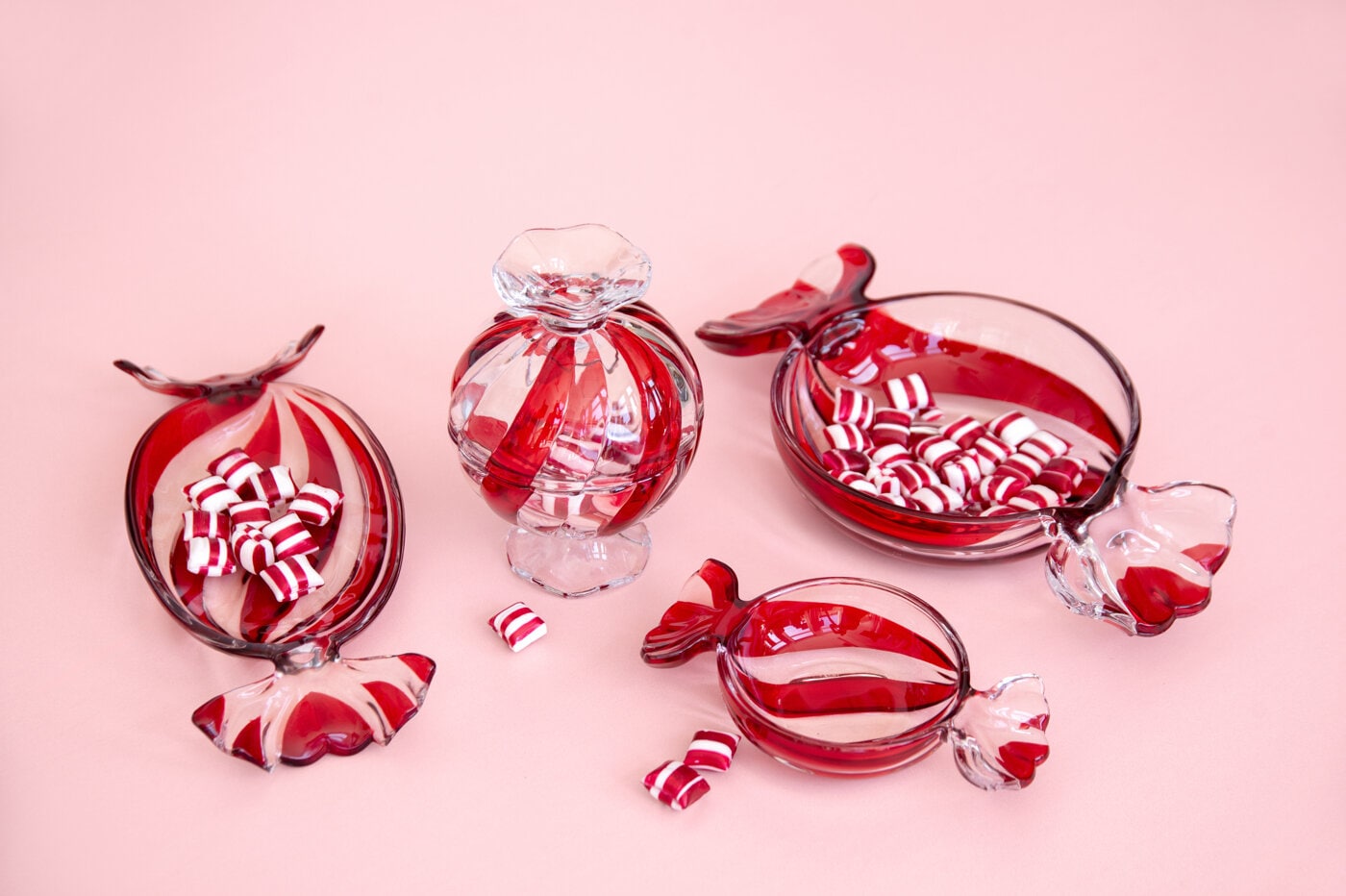 Godisfat formade som karameller i glas mot rosa bakgrund.