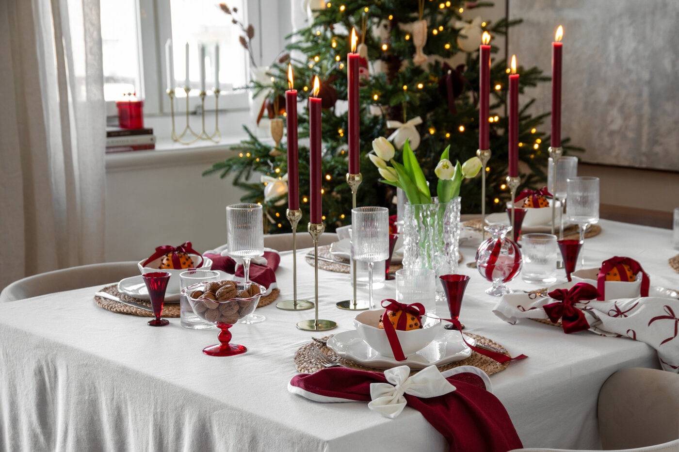 Juleborddekking i burgunder og hvitt med levende lys, glass og dekorative sløyfer.