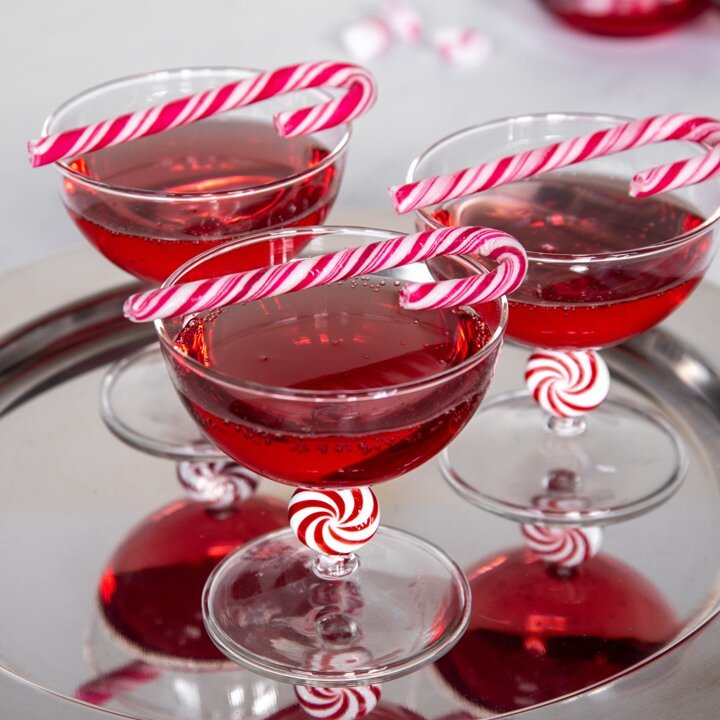 Cocktailglass med rød drikke og polkagriser som dekorasjon.