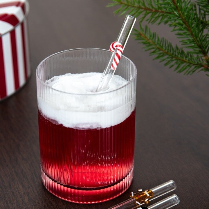 Ribbed drikkeglass med rød drikke, hvitt skum og glassugerør med polkagris.