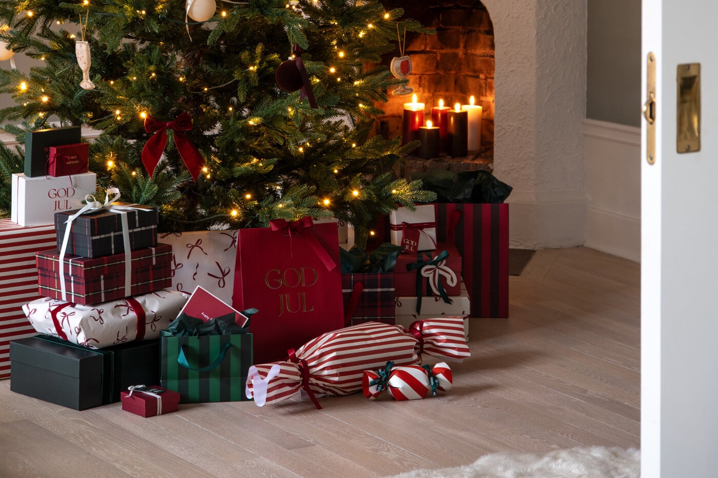 Inslagna julklappar placerade under en julgran framför en öppen spis.