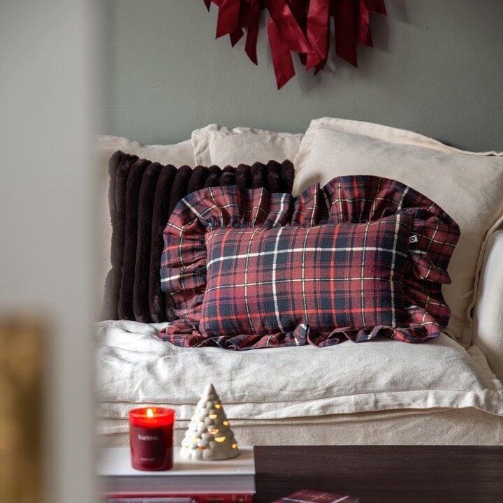 Julepyntet sofa med rutete puter, levende lys og dekorativt juletre.