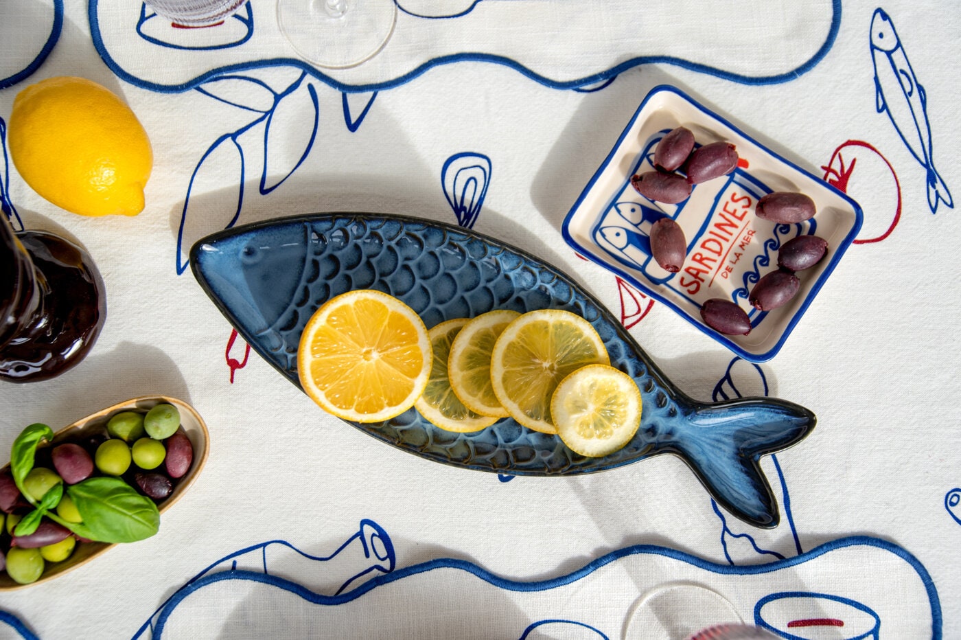 Fiskformet serveringsfat med sitronskiver på mønstret duk med oliven og småretter.