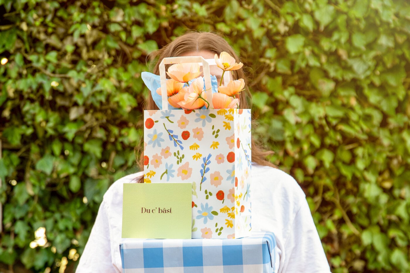 Person holder en blomstrete gavepose med blomster og kort