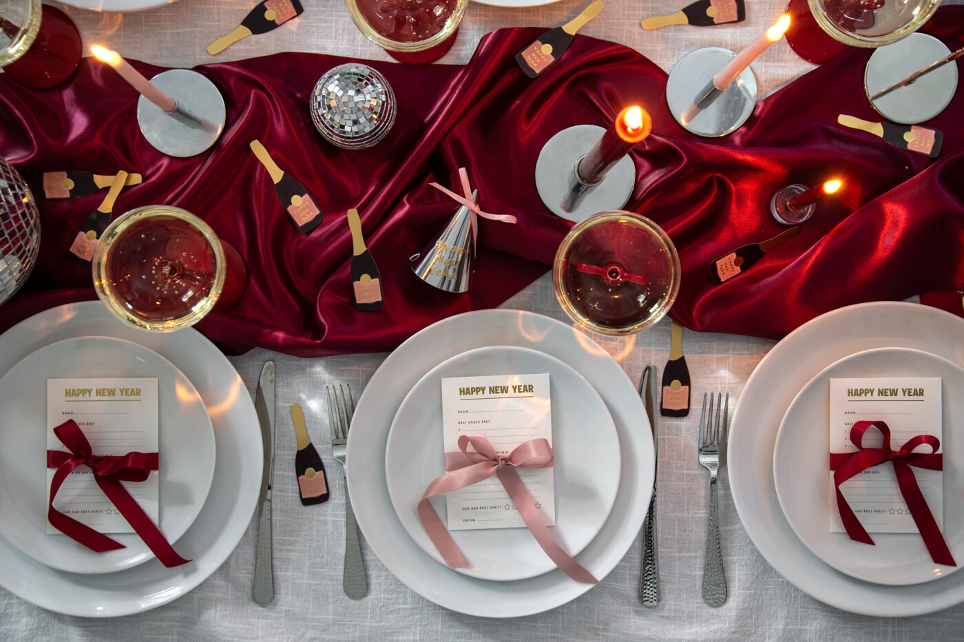 Nyårsdukning med vita tallrikar, röda ljus och partydekorationer på vit och röd duk.