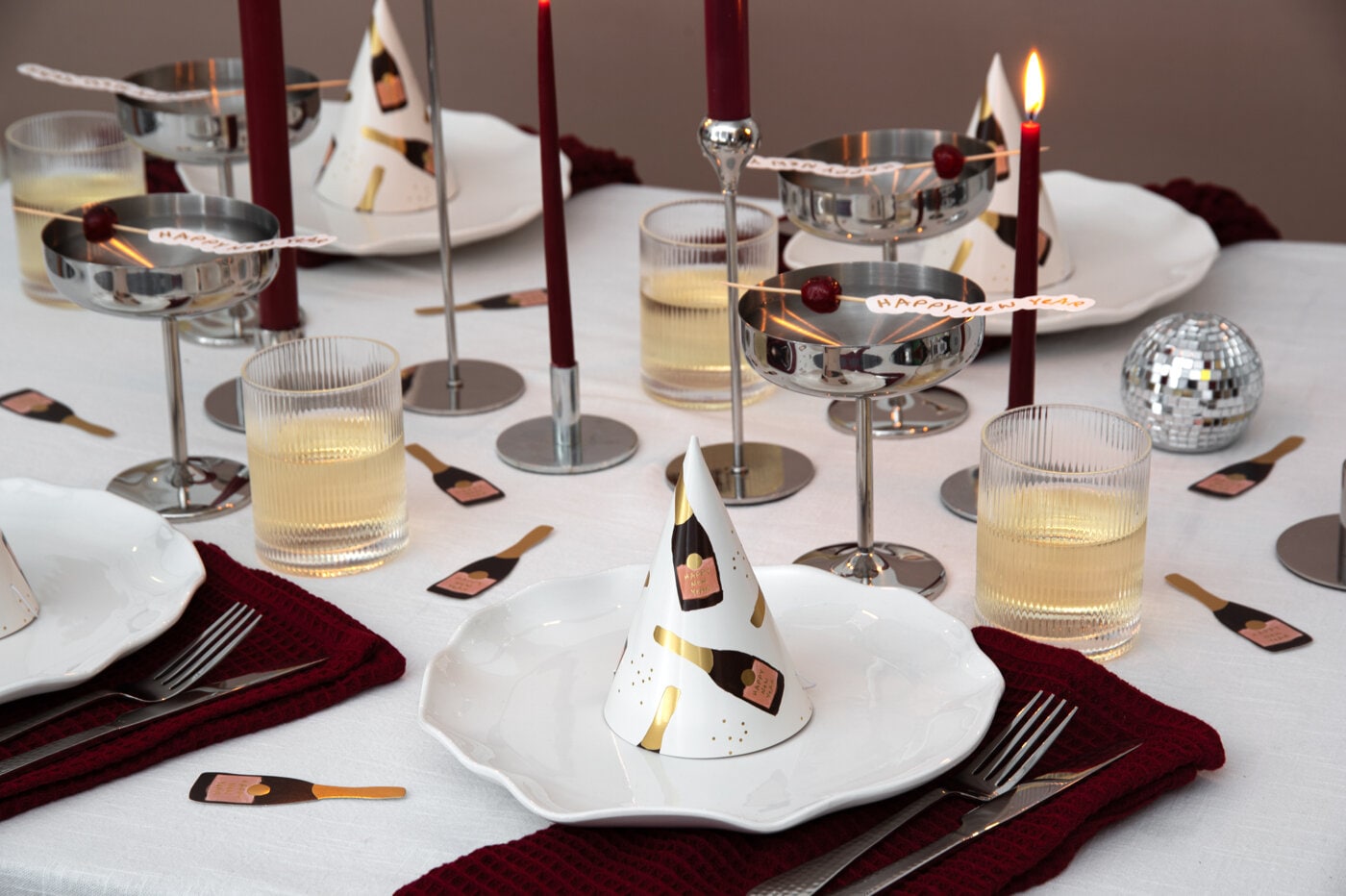 Nyårsdukning med champagneglas, röda ljus och partyhattar med flaskmotiv.
