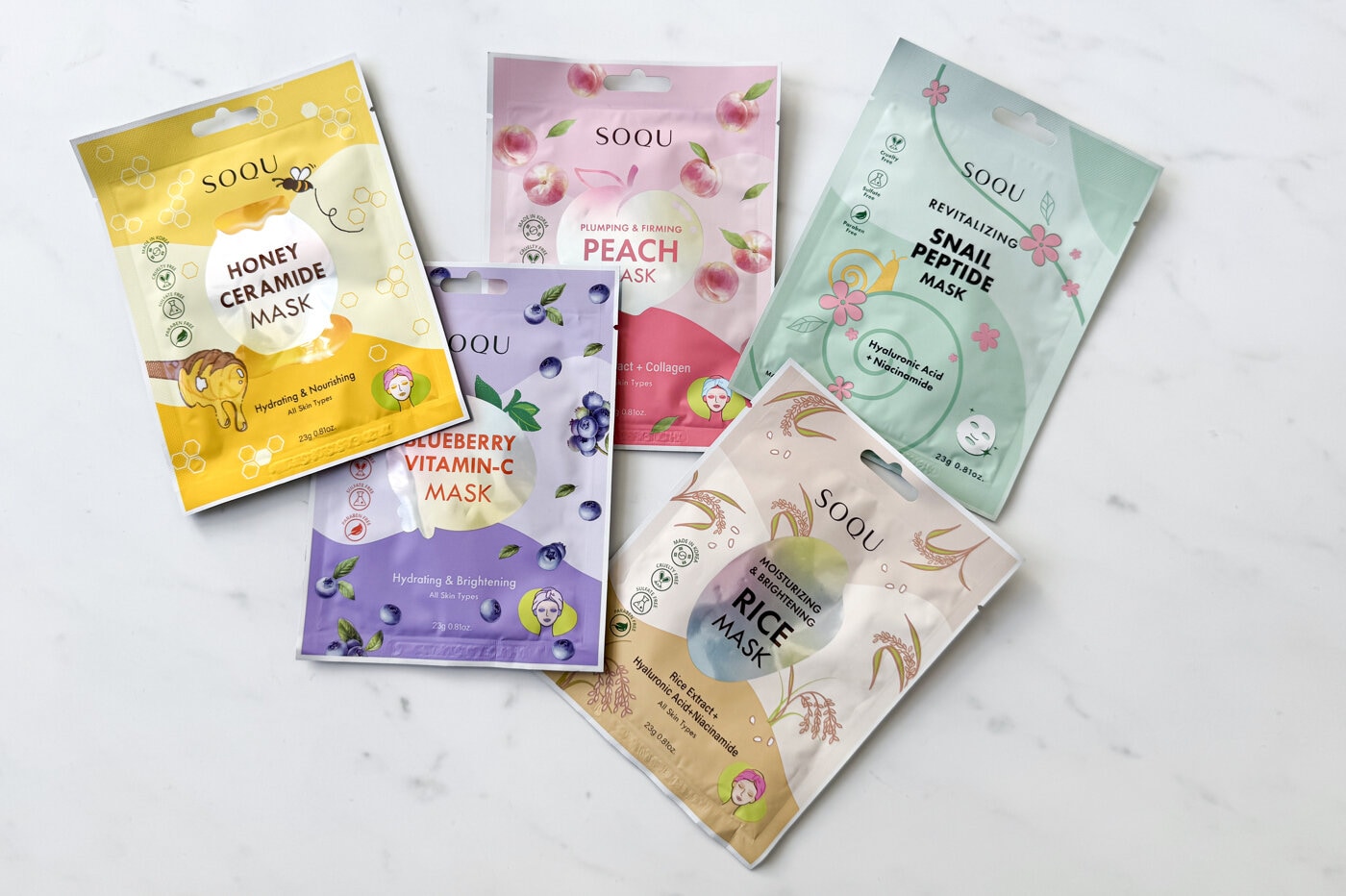 Flere fargerike pakninger av SOQU Sheet Masks – koreanske ansiktsmasker som fukter, roer og styrker huden.