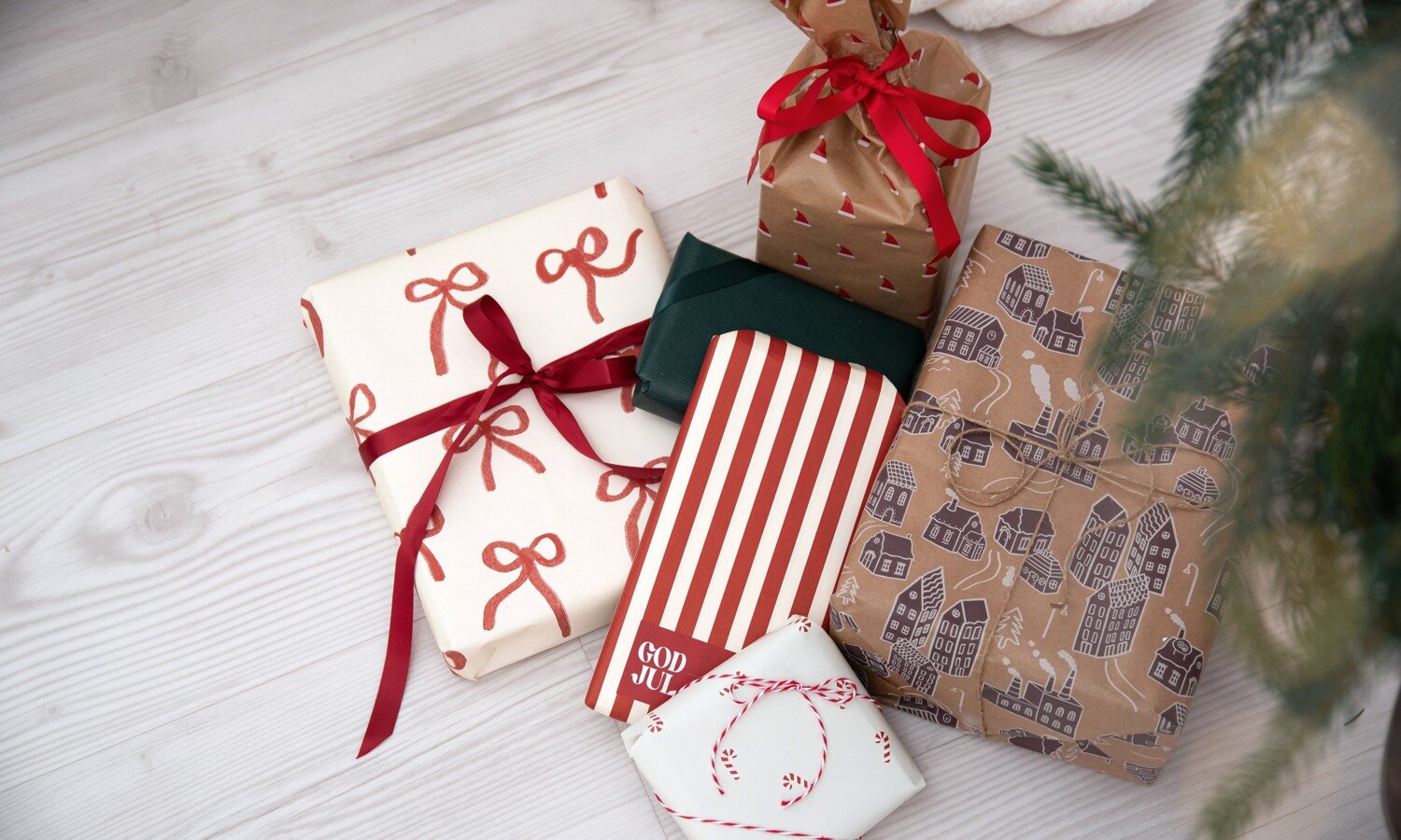 Julklappar inslagna i papper med rosetter, ränder och husmotiv med röda band.