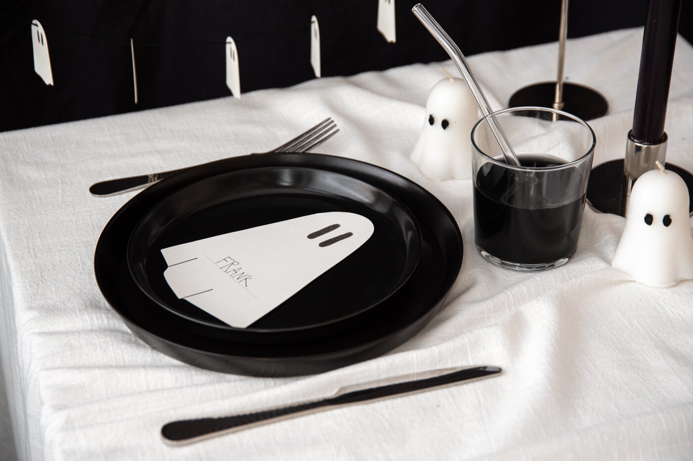 Halloweenborddekking med svarte tallerkener, spøkelseslys og svarte detaljer.